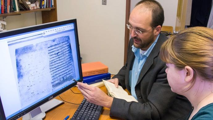 Dr. Dupertuis坐在一个指着电脑屏幕的学生旁边. 