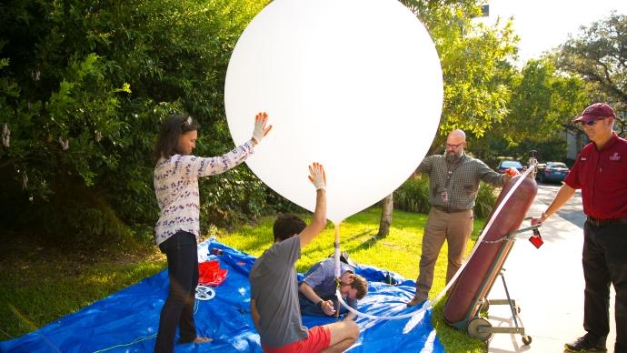 澳门金沙线上赌博官网 students and faculty work outdoors to fill a balloon with helium 