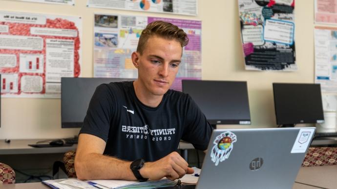 内森·布朗(Nathan Brown)看着Storch计算机实验室里的一台笔记本电脑，身后是学生的学术海报