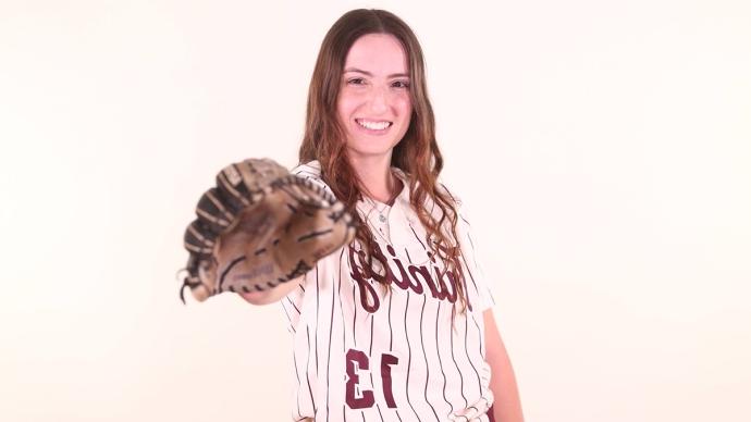 Jenna Kash stands in her softball uniform in front of a white background, holding out her gloved hand