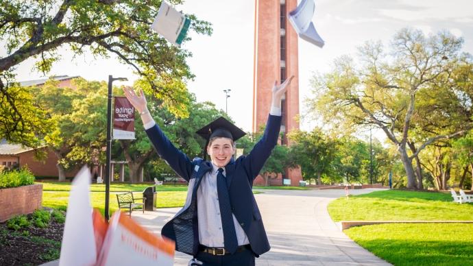 photo of recent graduate outside tossing books in the air and smiling