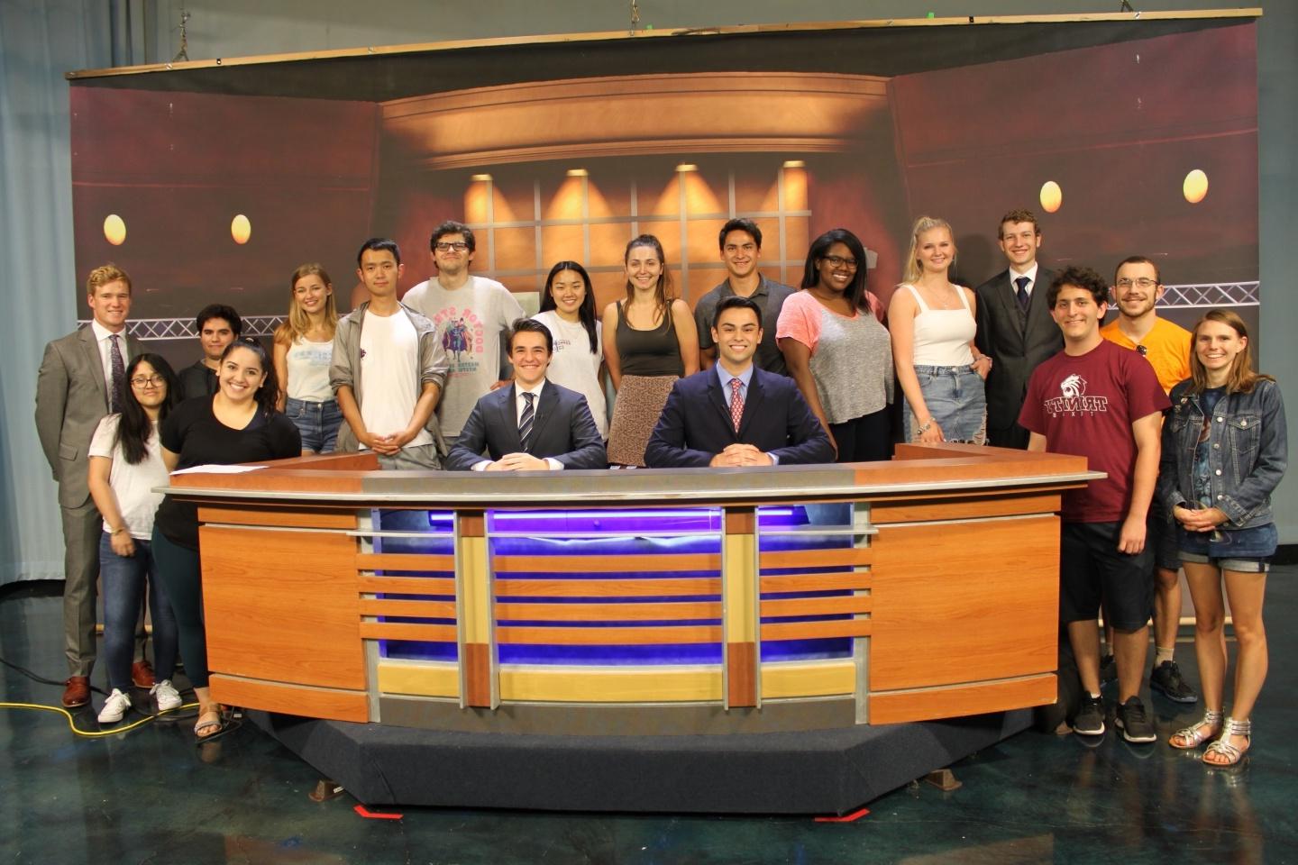 Newswave crew poses behind an anchor desk 