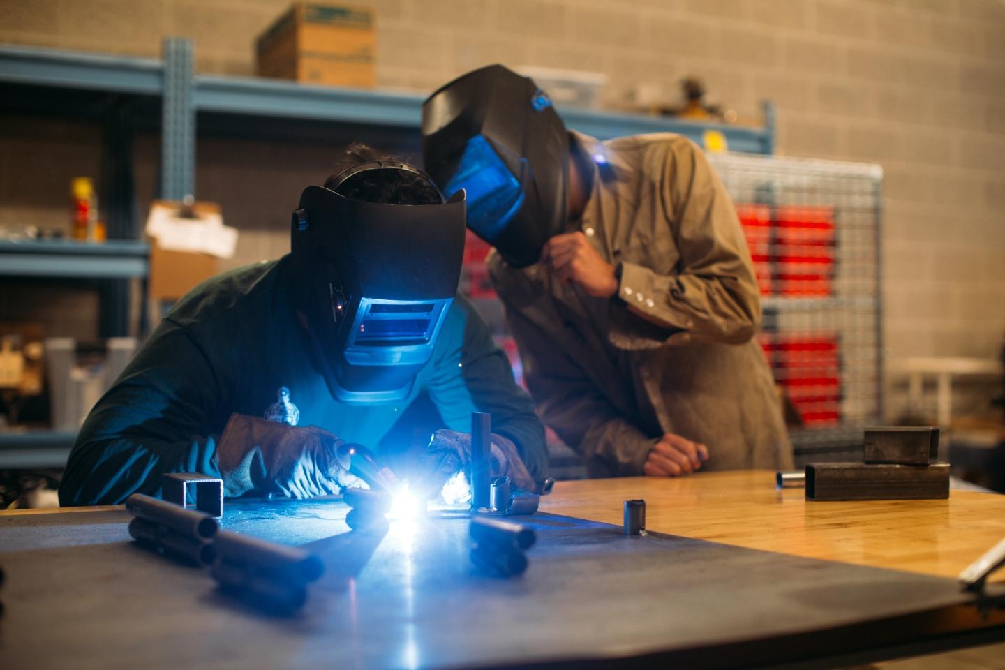 two students use a torch to weld metals