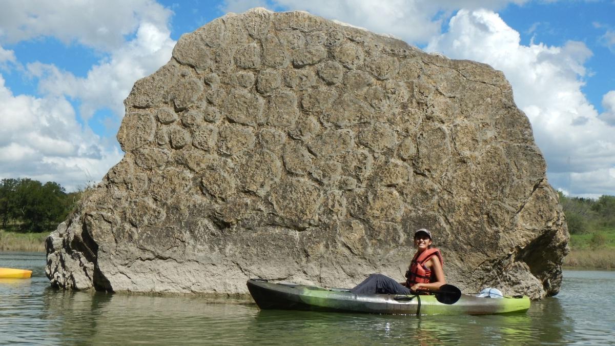 人在河中划着皮艇，身后是一块大石头作为风景