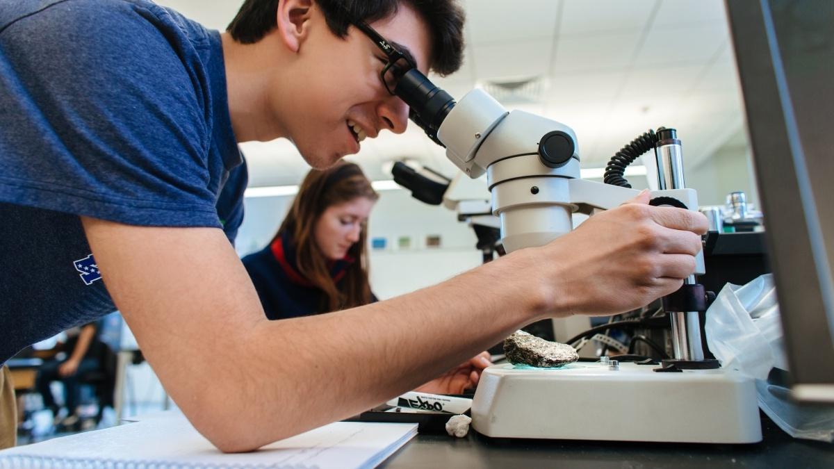 一个学生在看显微镜，背景是另一个学生