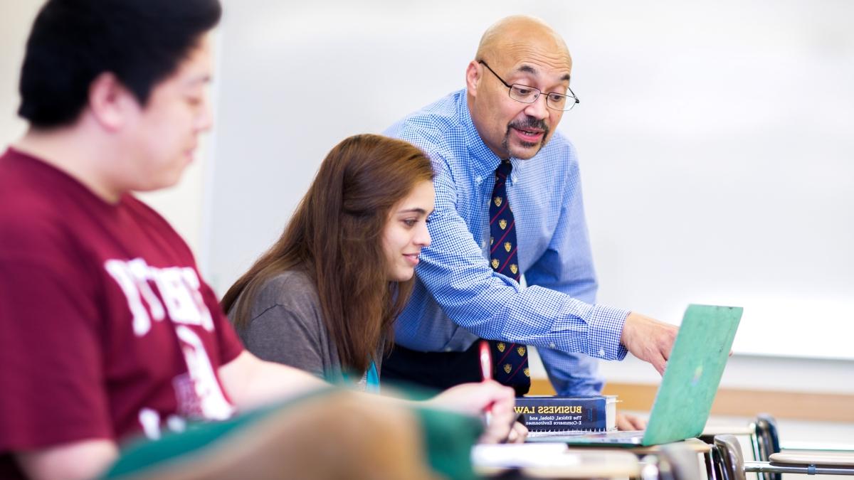 比利·伯克教授站在教室里的两个学生旁边, 指着其中一个笔记本电脑的屏幕